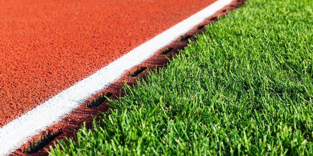 Symbolfoto für den Blogbeitrag „Was kostet ein Kunstrasenplatz?”, Detailaufnahme Tartanbahn neben Kunstrasen