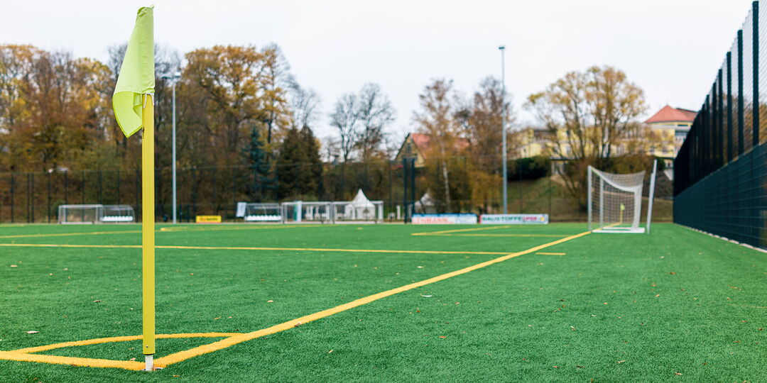 Detailaufnahme Kunstrasen mit gelber Eckfahne, Symbolfoto für den Blogbeitrag „Kunstrasen vs. Naturrasen?”,