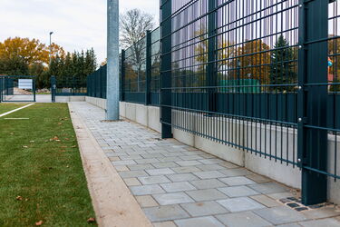 Gepflasterter Bereich zwischen Spielfeld und Zaun