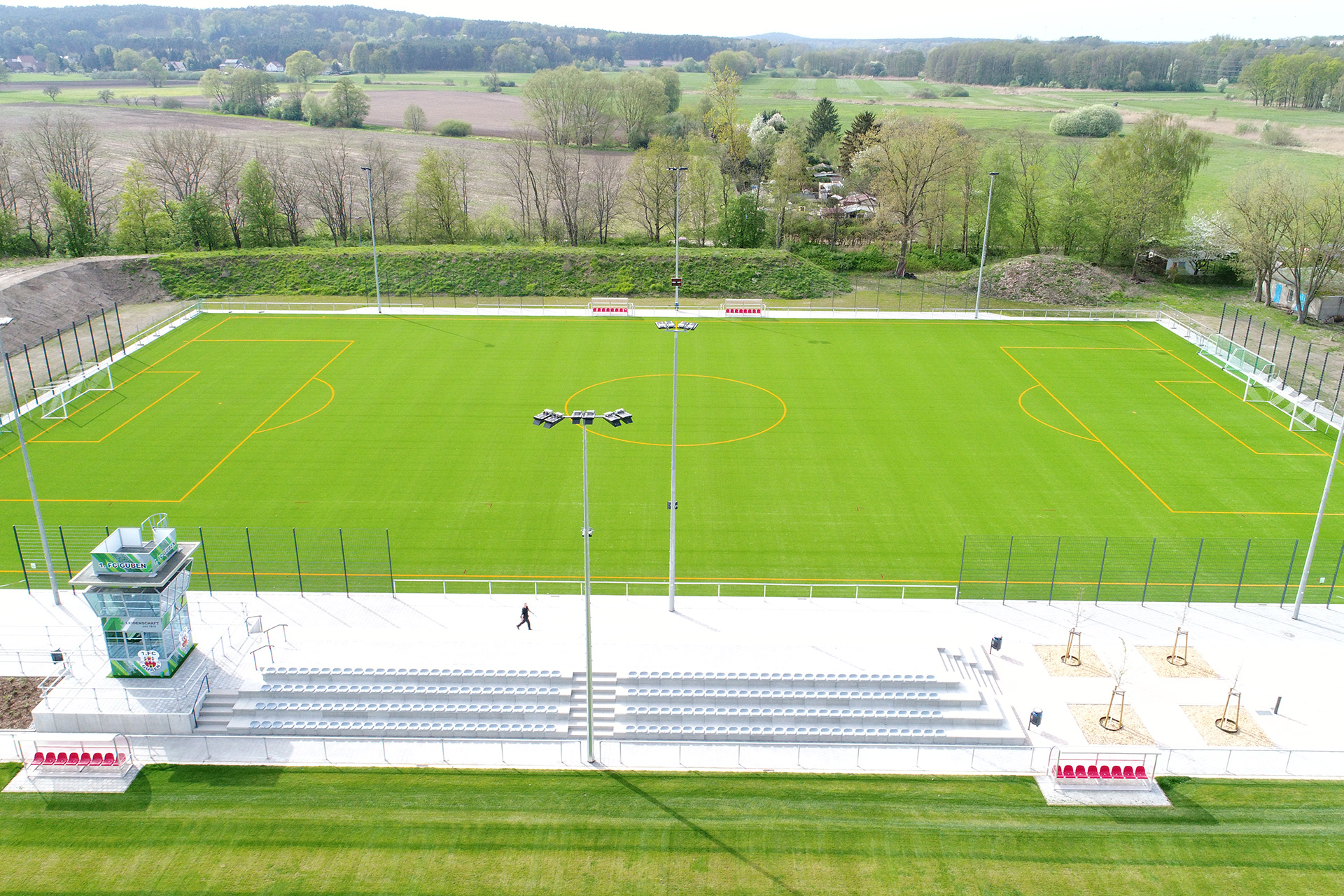 Moderne FSportanlage Kaltenborner Straße Guben mit einem neuen Kunstrasen und Tribünen, umgeben von einer malerischen Landschaft.